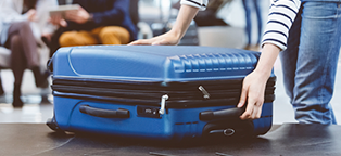 a man or women picking up a blue suite case from a conveyor belt 