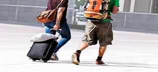 two men walking toward a building with backpacks and a suitcase 