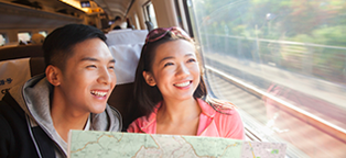 young man and woman on train holding map smiling while looking out of the window