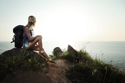 Woman with backpack sitting on rock looking at sunset over ocean