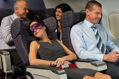 woman sleeping on plane with eye mask with other passengers seated near her