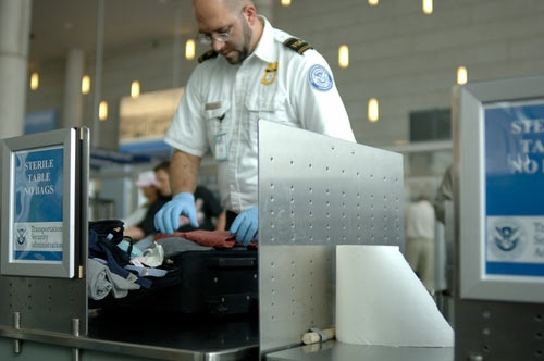 TSA agent looking through luggage at an airport security check point